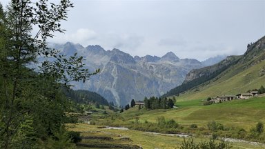 Weitläufige alpine Landschaft mit grünem Vordergrund und majestätischen, bewölkten Berggipfeln.